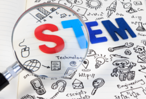 A magnifying glass is focused on the first two letters of the STEM acronym, which is surrounded by small doddles of science-related objects, such as robots or beakers from a lab